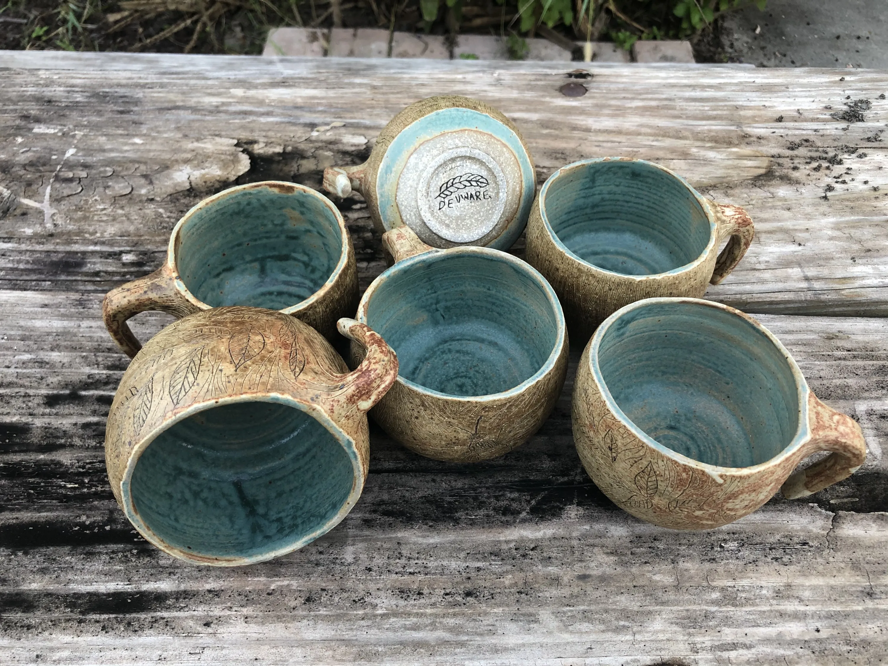 Six hand-thrown ceramic mugs with carved exteriors and blue-green glaze